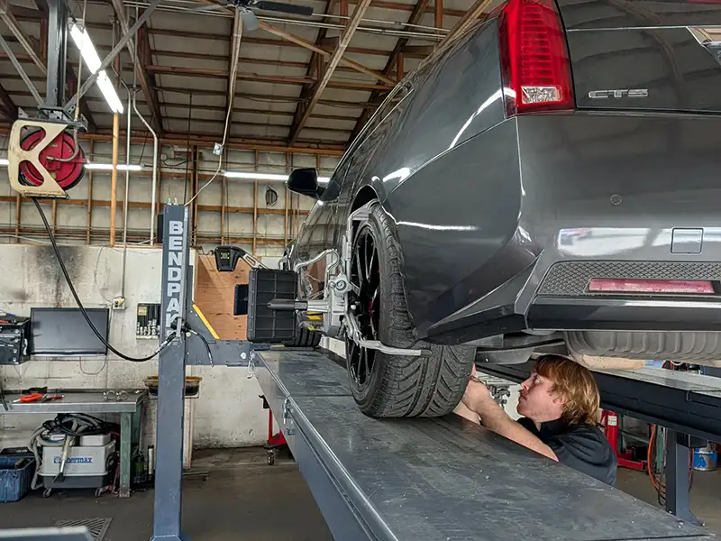 Marysville Auto Maintenance Technician Under Vehicle Technician performing vehicle maintenance inspection underneath a car on a lift at NorthState Auto Clinic.